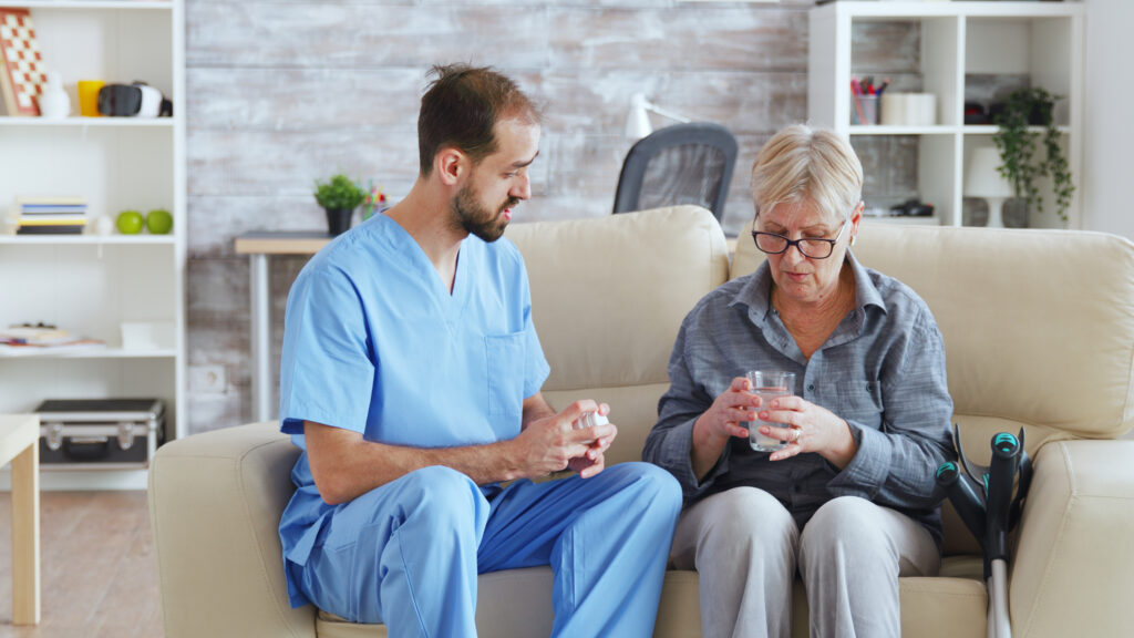 male nurse sitting on couch with senior woman giving her medical treatment in nursing home