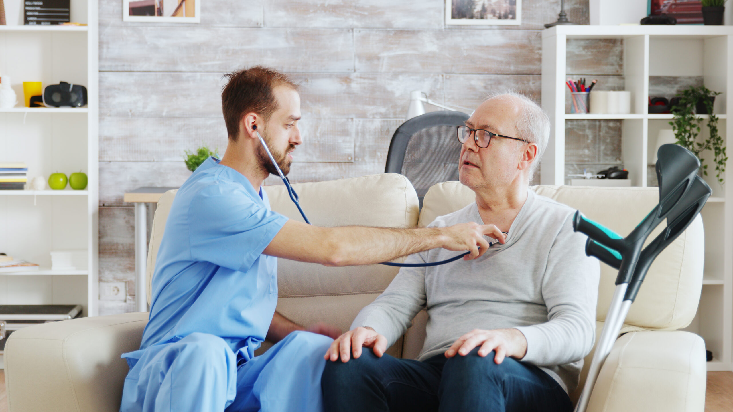 revealing shot young male nurse listening old retired man heartbeat bright cozy nursing home caregiver social worker